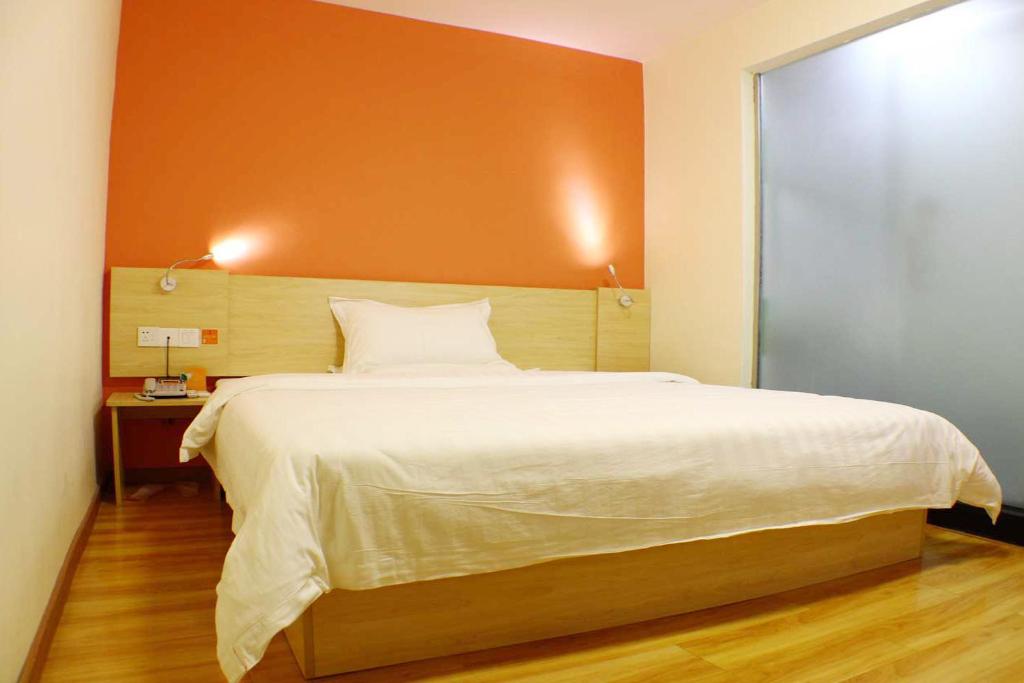 a bedroom with a large bed with an orange wall at 7Days Inn Shaoguan Renhua Mount Danxia in Shaoguan