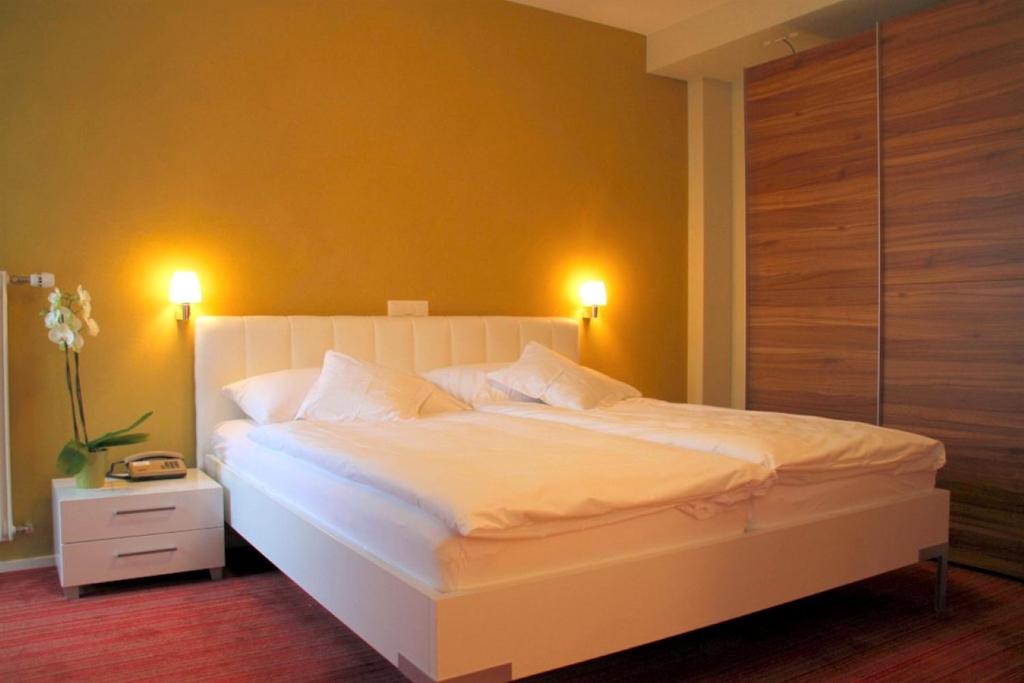 a bedroom with a large white bed with two lights at Hotel Berghof Amaranth in Wilderswil