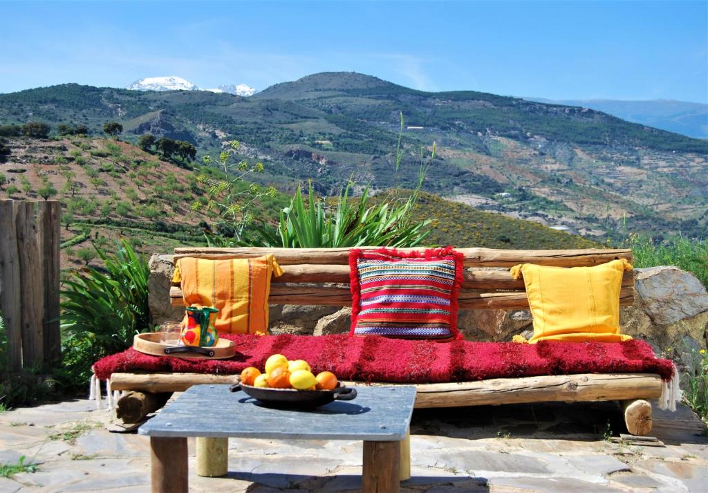 un banco de madera con almohadas y un bol de fruta en una mesa en Cortijo Los Maximos, en Turón