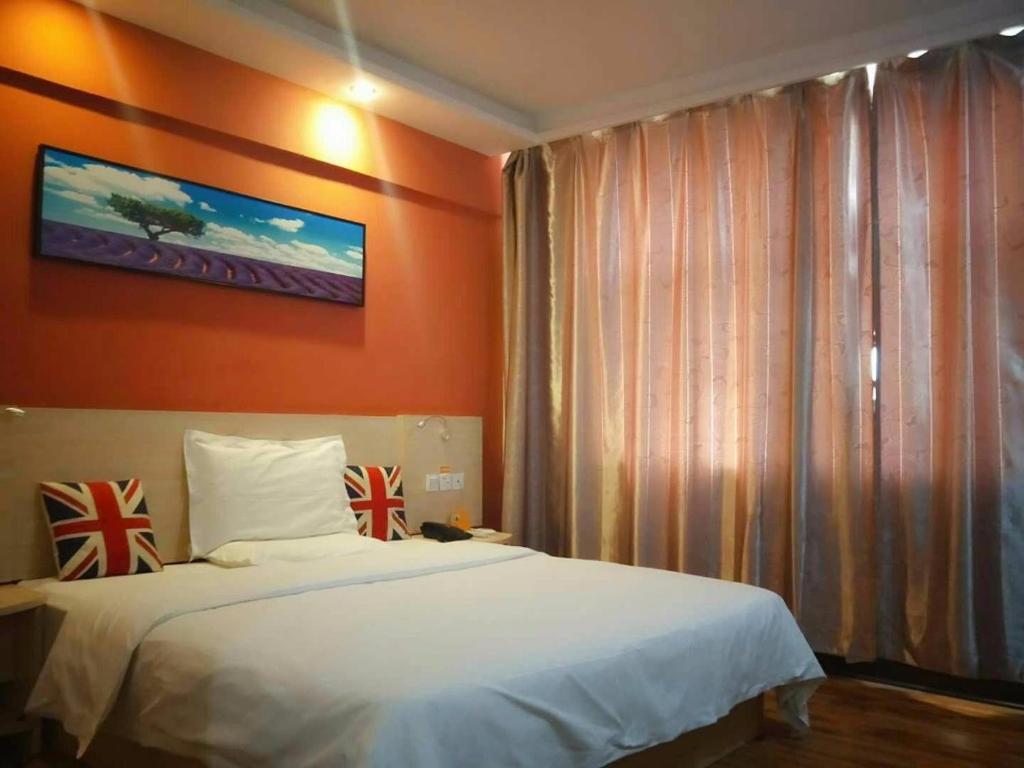 1 dormitorio con cama blanca y pared de color naranja en 7Days Inn Linhe Railway Station, en Bayannur