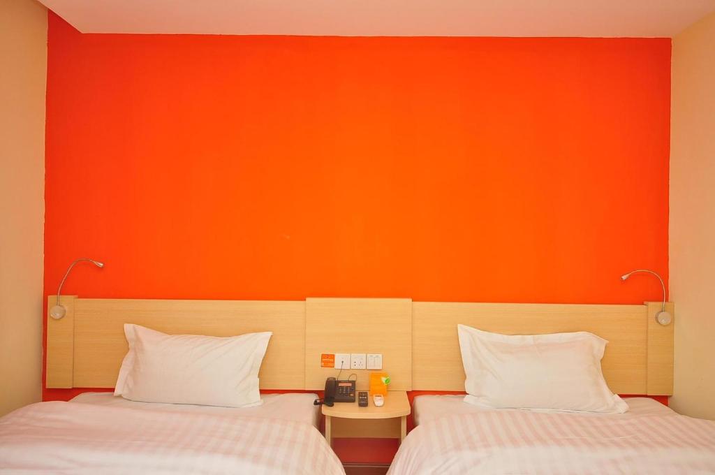 2 camas en una habitación con pared de color naranja en 7Days Inn Dezhou Qihe Coach Terminal, en Huadian