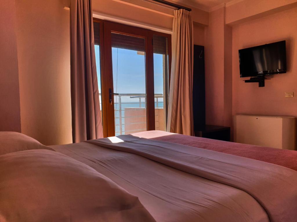 Schlafzimmer mit einem Bett mit einem Fenster und einem TV in der Unterkunft Hotel Nais Beach in Durrës