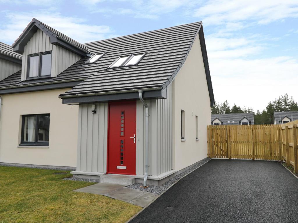 a white house with a red door and a fence at 3 Osprey Drive in Boat of Garten