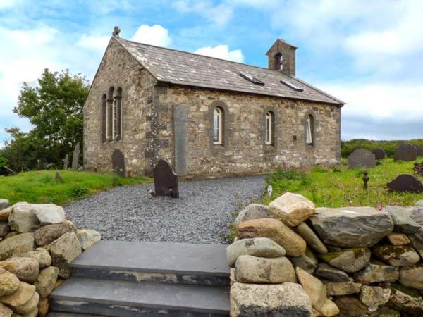 una vieja iglesia de piedra con una pared de piedra delante de ella en Eglwys St Cynfil, en Pwllheli