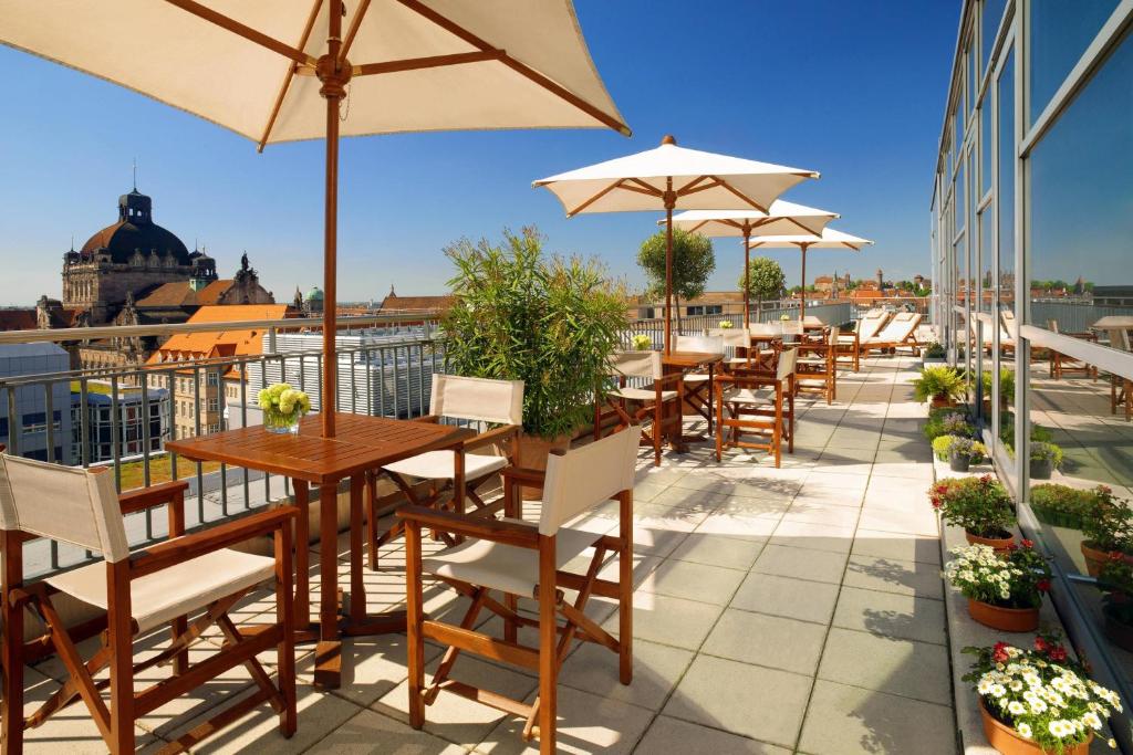 eine Terrasse mit Tischen und Sonnenschirmen auf dem Dach in der Unterkunft Sheraton Carlton Nuernberg in Nürnberg