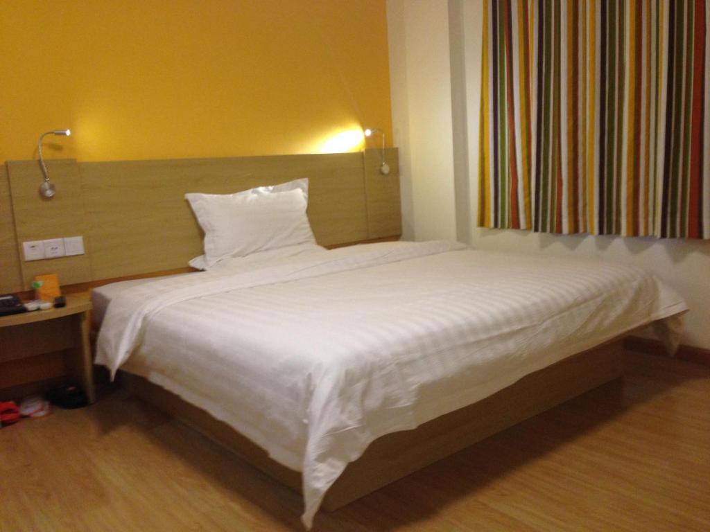 a bed in a hotel room with a white comforter at 7Days Inn Anji Centre in Huzhou