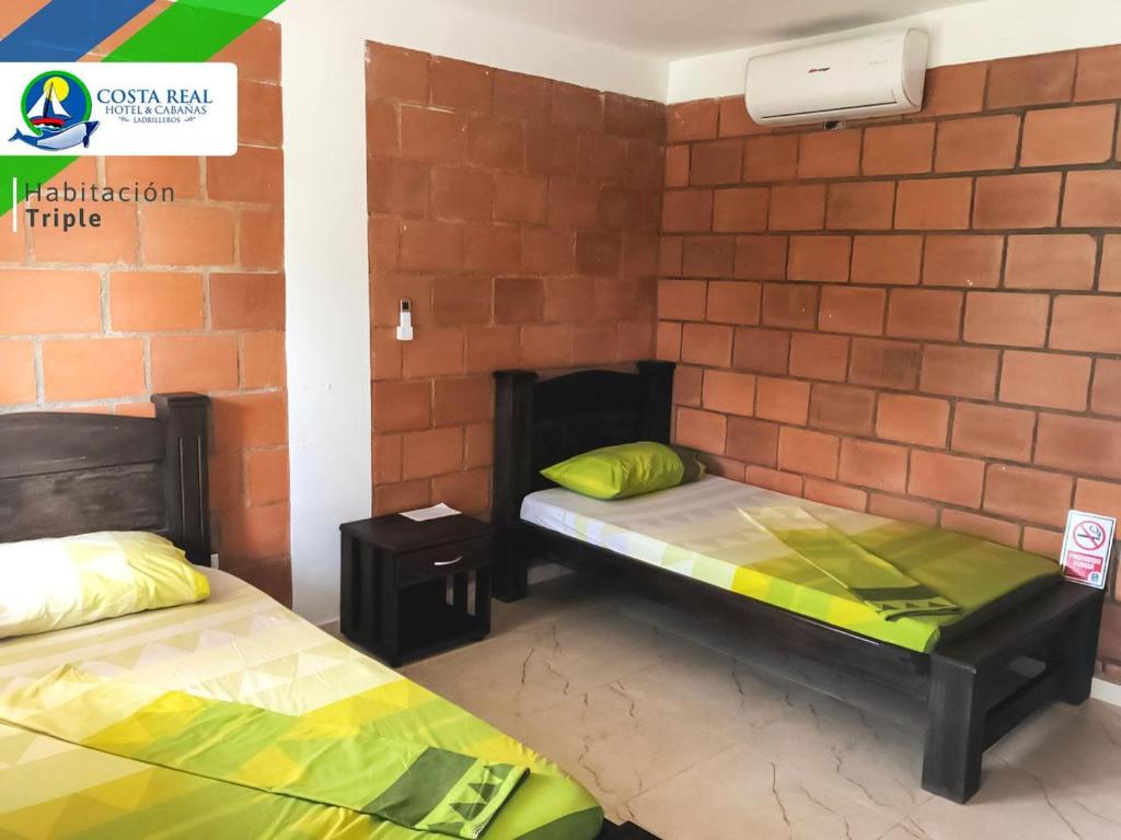 2 camas en una habitación con una pared de ladrillo en Hotel Costa Real, en Playa Ladrilleros