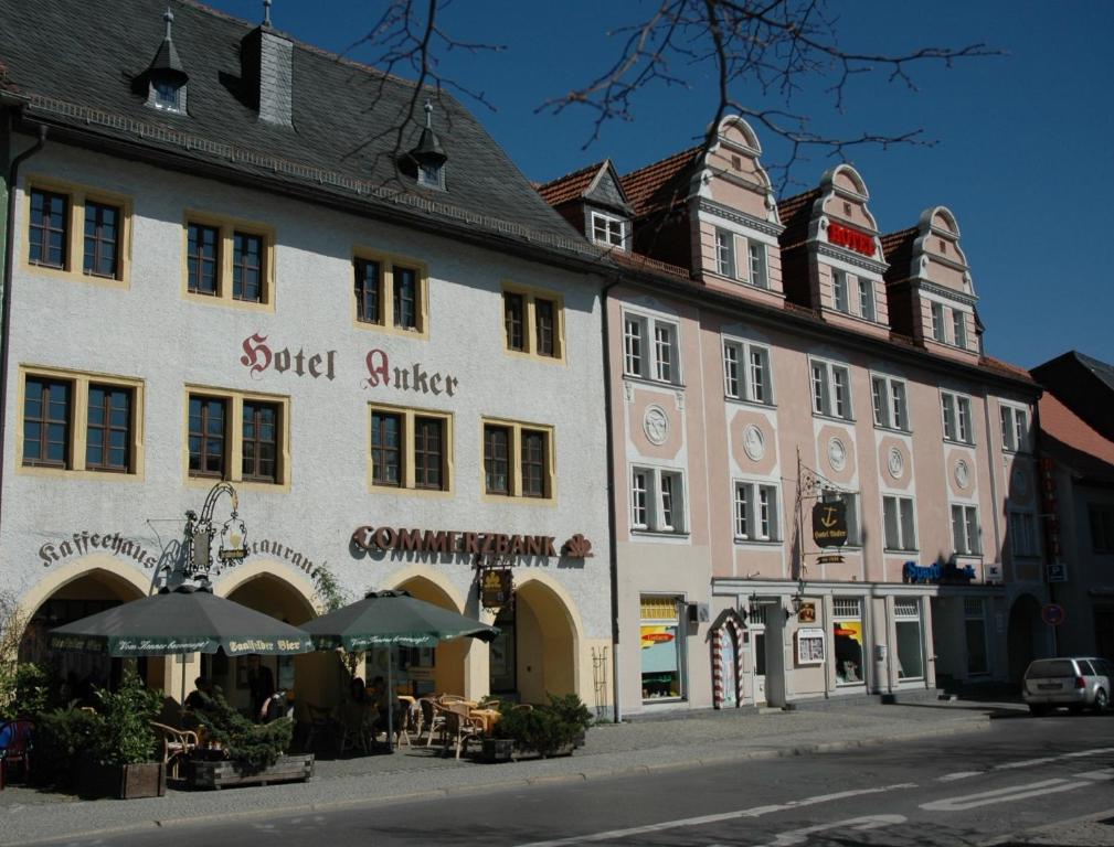 ein großes weißes Gebäude mit Sonnenschirmen auf einer Straße in der Unterkunft Hotel Anker in Saalfeld