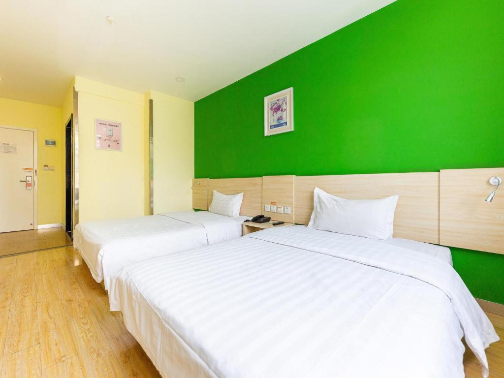 2 łóżka w pokoju z zieloną ścianą w obiekcie 7Days Inn Xining Kunlun Road Cross w mieście Xining