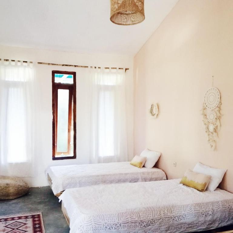 two beds in a room with white walls and a window at Lambo home stay in Waikabubak