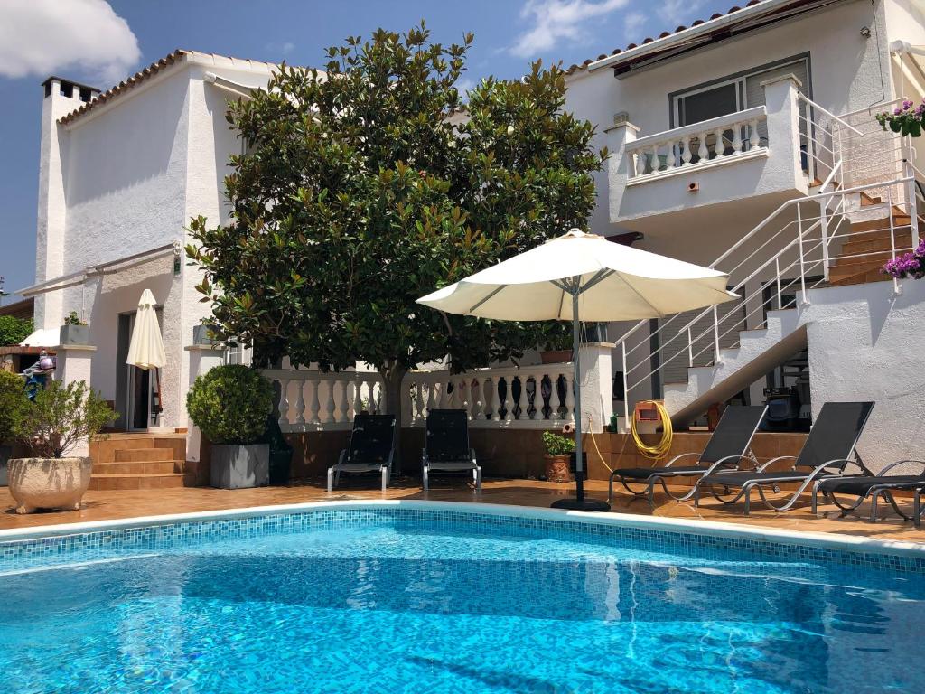 a swimming pool with chairs and an umbrella next to a house at Casa Pani in Empuriabrava