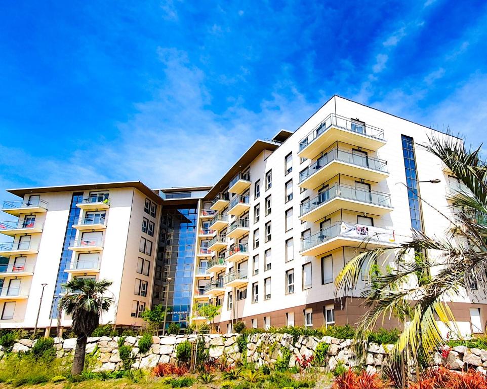 un grand bâtiment blanc avec des palmiers devant lui dans l'établissement Domitys Le Jardin Des Palmiers, à Ajaccio