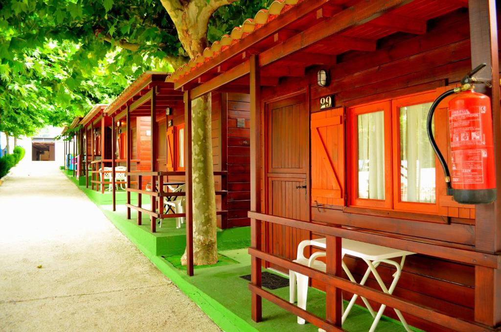 a row of wooden cabins with tables and chairs at Camping Playa Canelas in Portonovo