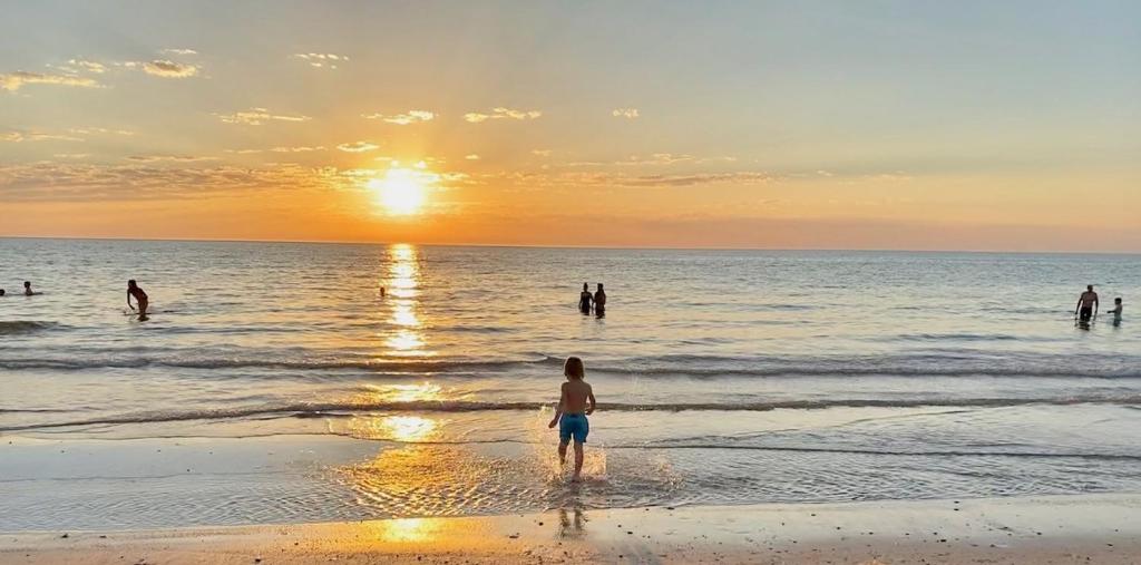 uma pessoa de pé na praia ao pôr do sol em Atlantic West Beach Apartments em Adelaide