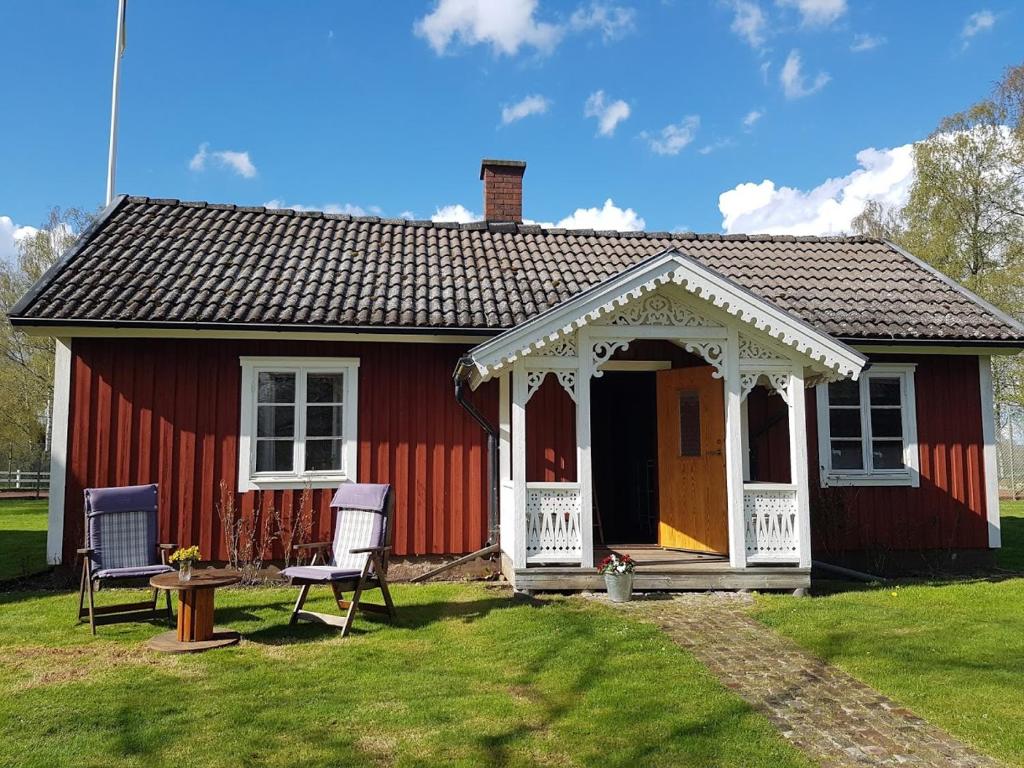ein rotes Haus mit einer weißen Veranda und 2 Stühlen in der Unterkunft Lillastugan Sätuna in Falköping