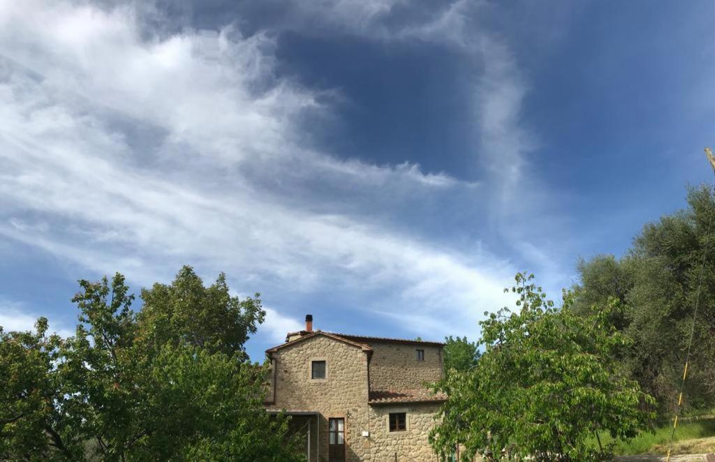 a stone house with trees in front of a cloudy sky at Giardino di Potentino in Seggiano