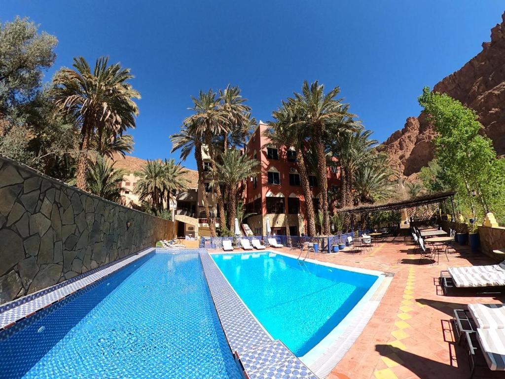 a swimming pool with palm trees and a building at Kasbah Restaurant Amazir in Tinerhir