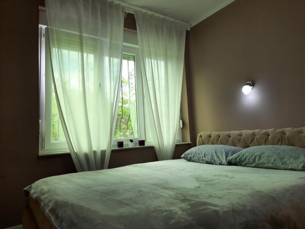 a bedroom with a bed and a window with white curtains at Apartman Nana in Mostar