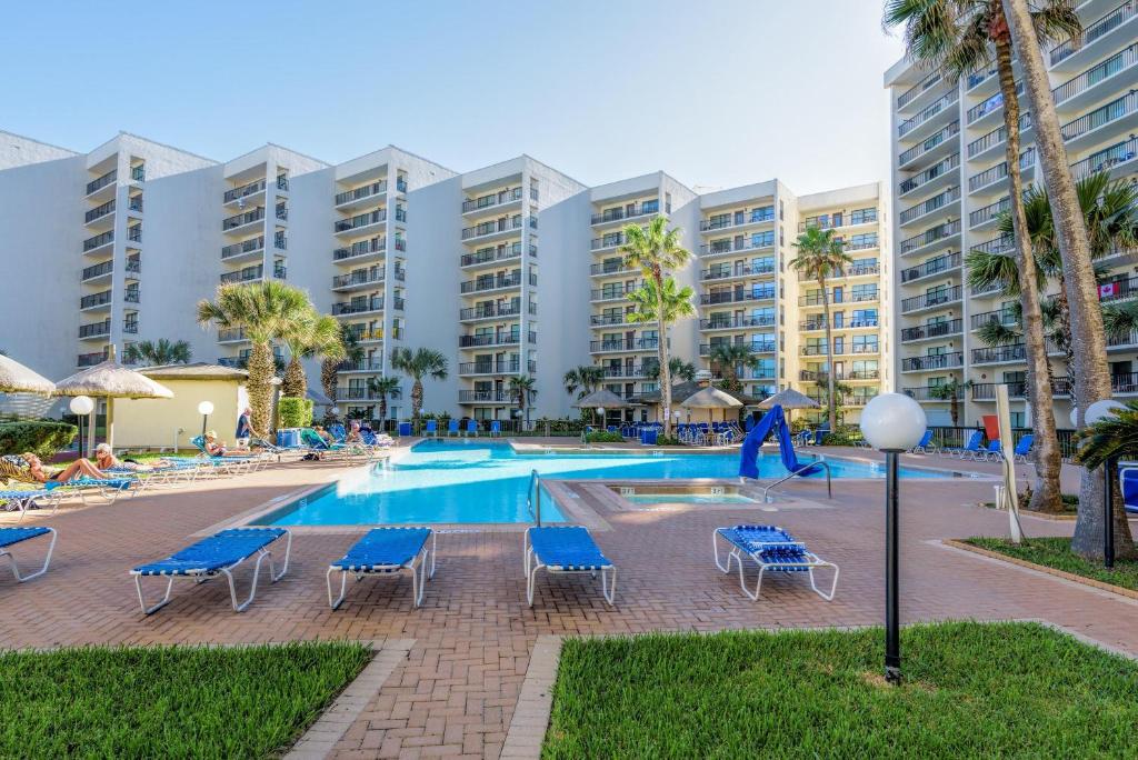 una piscina en un complejo con sillas azules y palmeras en Beachfront luxury condo with all the resort amenities! en South Padre Island