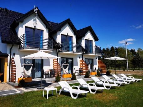 eine Reihe von weißen Stühlen und Sonnenschirmen vor einem Haus in der Unterkunft Holiday Amber - in Niechorze