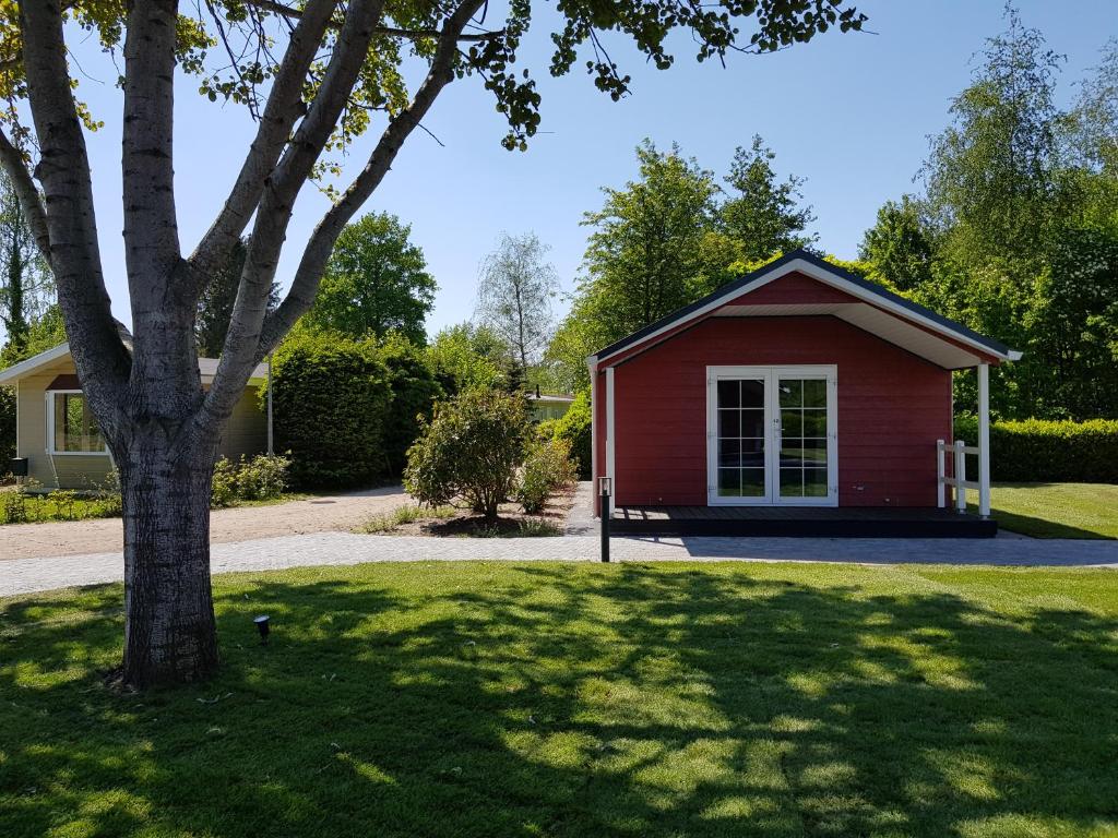 a red house with a tree in a yard at De Bijsselse Enk, Noors chalet 12 in Nunspeet