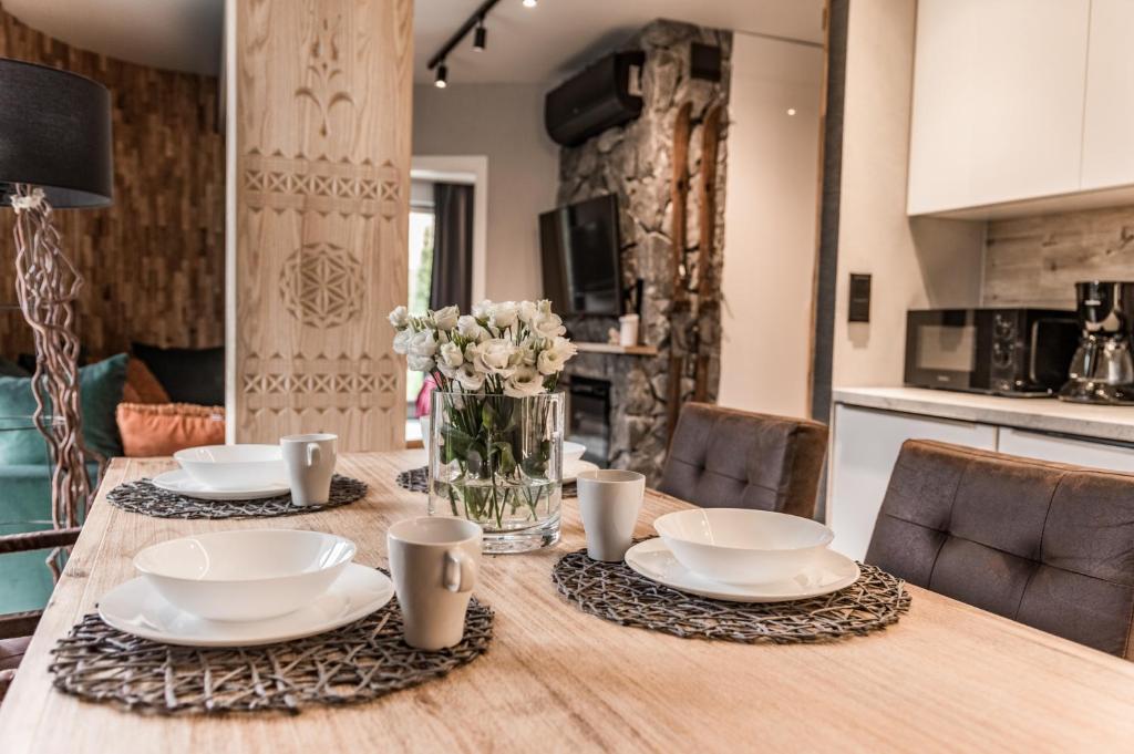 a wooden table with plates and cups and flowers on it at Apartamenty Comfort & Spa Stara Polana in Zakopane
