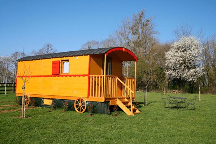 un vagón de tren amarillo y rojo sentado en un campo en Roulotte Poulette, en Mortagne-au-Perche