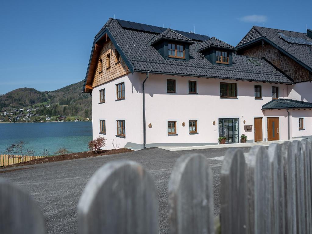 a white house with a fence next to a lake at Brunnwirt ESSEN & WOHNEN in Fuschl am See