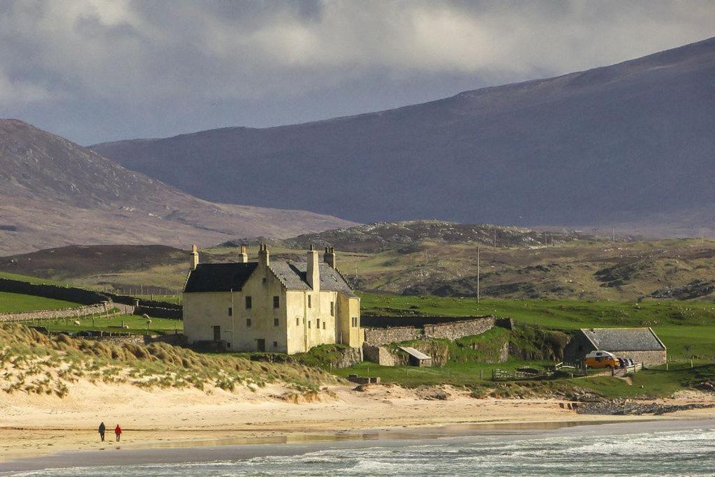 a building on a beach next to the ocean at Balnakeil House in Balnakeil