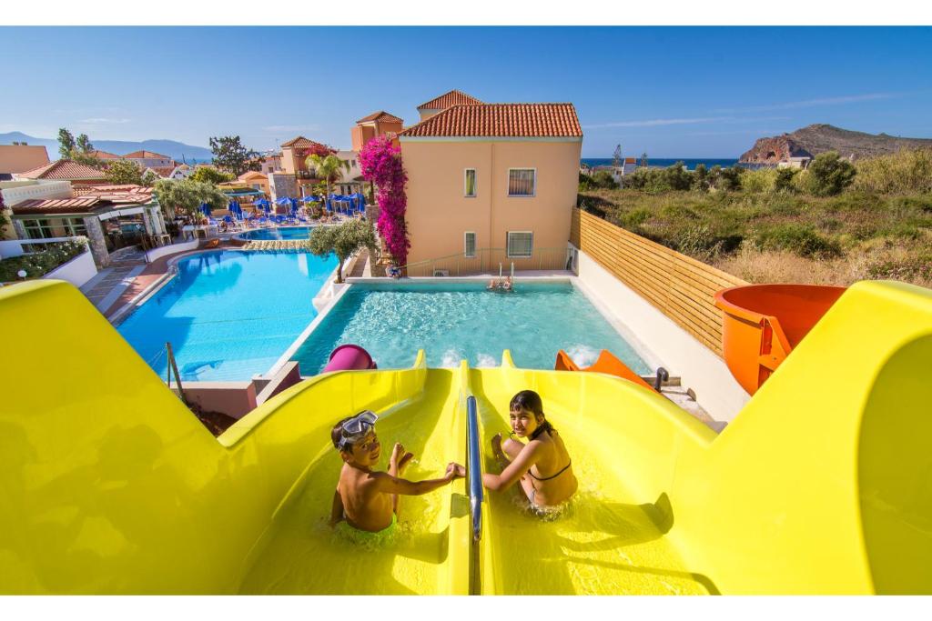 duas pessoas num escorrega aquático numa piscina em Stefan Village Hotel em Agia Marina Nea Kydonias