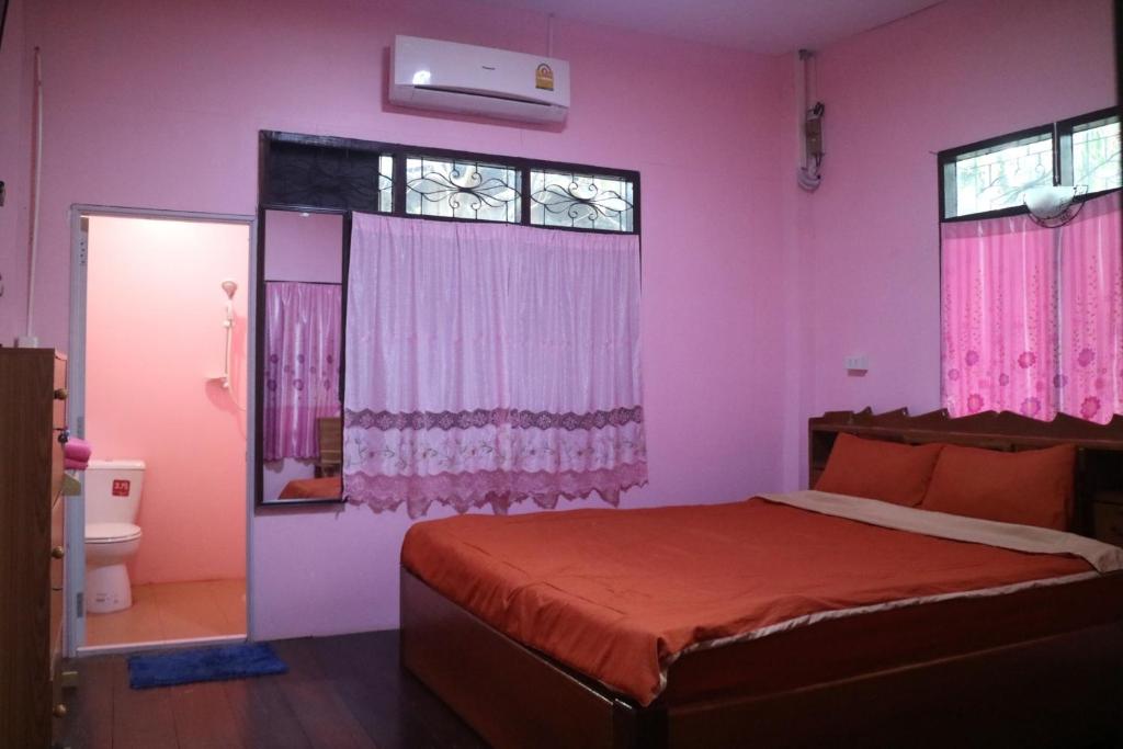 a bedroom with a bed with pink walls and windows at Baanmakpoo บ้านหมากพลู in Sangkhla Buri