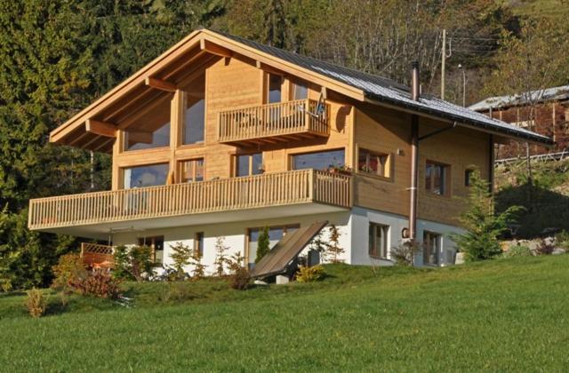 a large wooden house with a balcony in a field at Chalet Lyngen in Leysin
