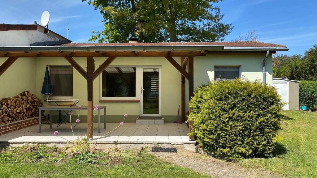 ein kleines gelbes Haus mit einer hölzernen Pergola in der Unterkunft Ferienhaus Bungalow in Arendsee in ruhiger Lage in Arendsee