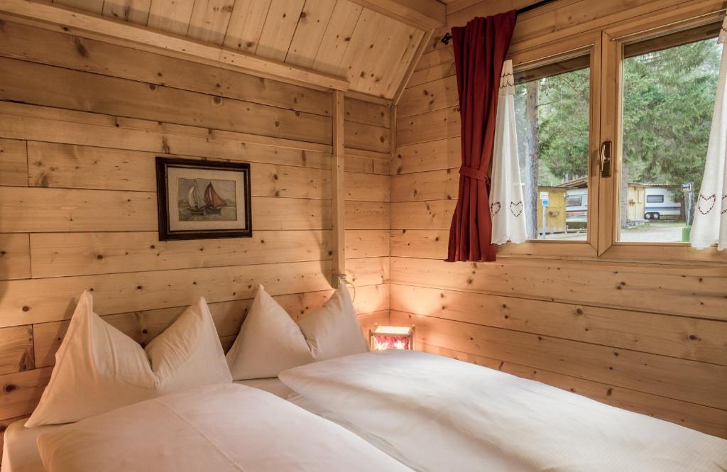 1 dormitorio con paredes de madera y 1 cama con almohadas blancas en Camping Sass Dlacia, en San Cassiano