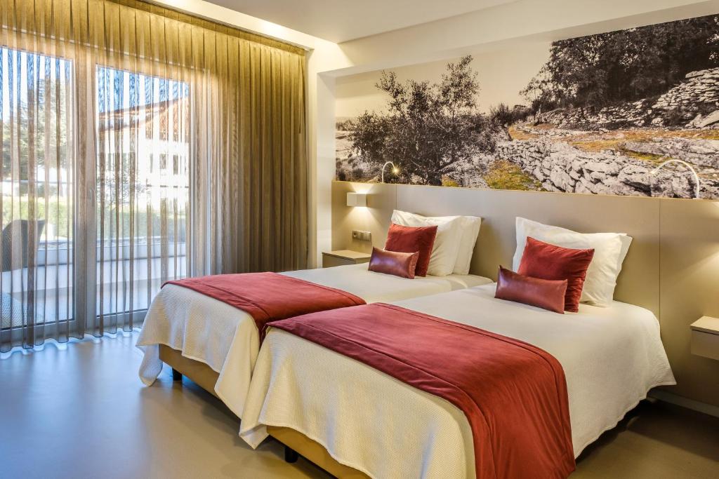 two beds in a hotel room with a large window at Hotel Serra d'Aire - Boutique Hotel in Fátima