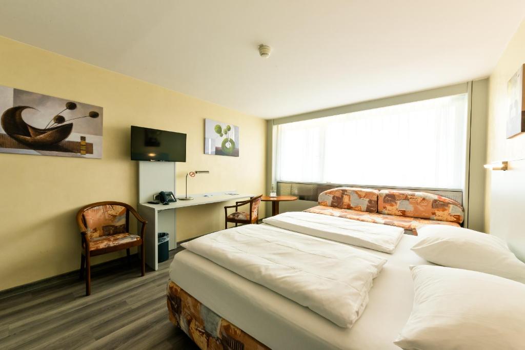 a bedroom with two beds and a desk and a window at City Hotel Heilbronn in Heilbronn