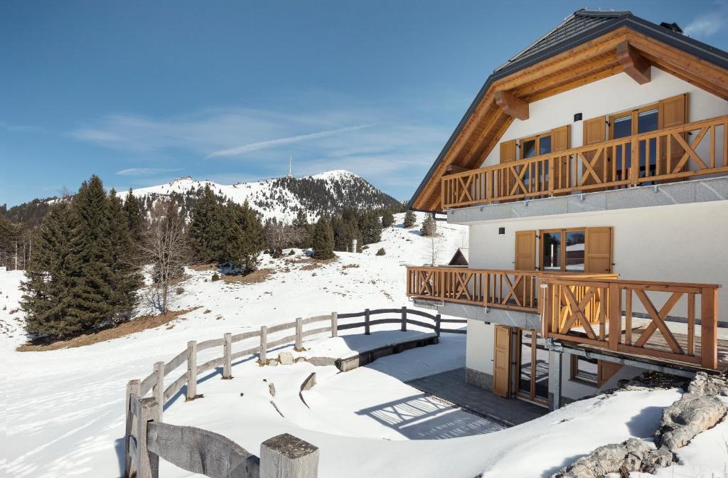 una casa di tronchi nella neve con una terrazza in legno di Apartment Jezerca - Krvavec a Cerklje na Gorenjskem