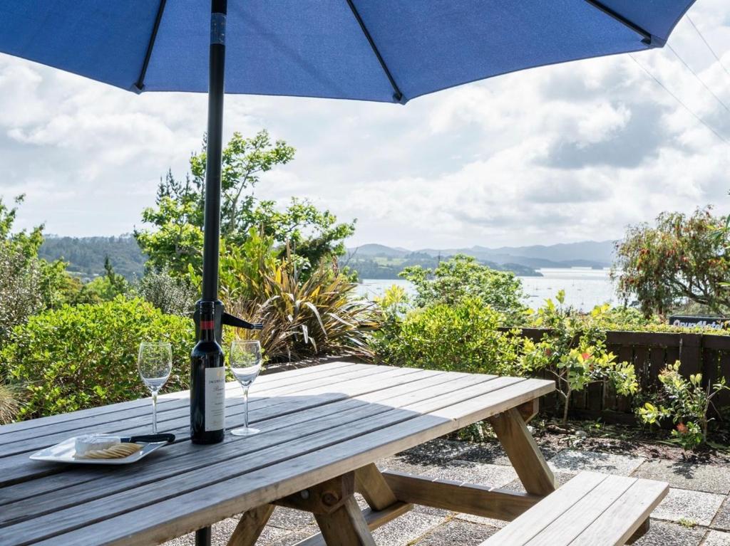 een picknicktafel met een blauwe parasol en wijnglazen bij Blue Peter - Opua Holiday Home in Opua