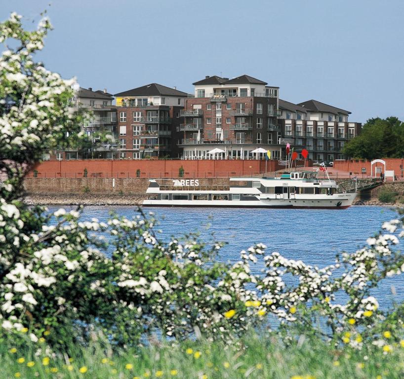 ein Boot auf einem Fluss mit Gebäuden im Hintergrund in der Unterkunft Hotel Rheinpark Rees in Rees