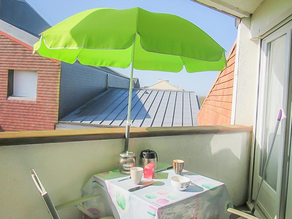 una mesa con una sombrilla verde en el balcón en Cabourg, cosy appartement avec balcon + parking privé, en Cabourg