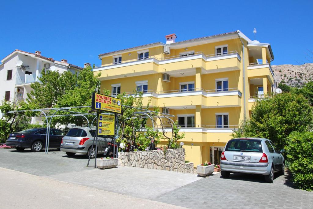 un edificio amarillo con coches estacionados en un estacionamiento en Apartments Brnic, en Baška