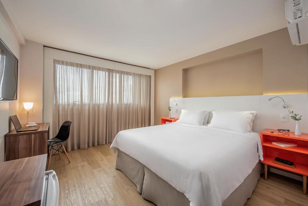 Habitación de hotel con cama blanca grande y escritorio. en Intercity Curitiba Centro Cívico, en Curitiba