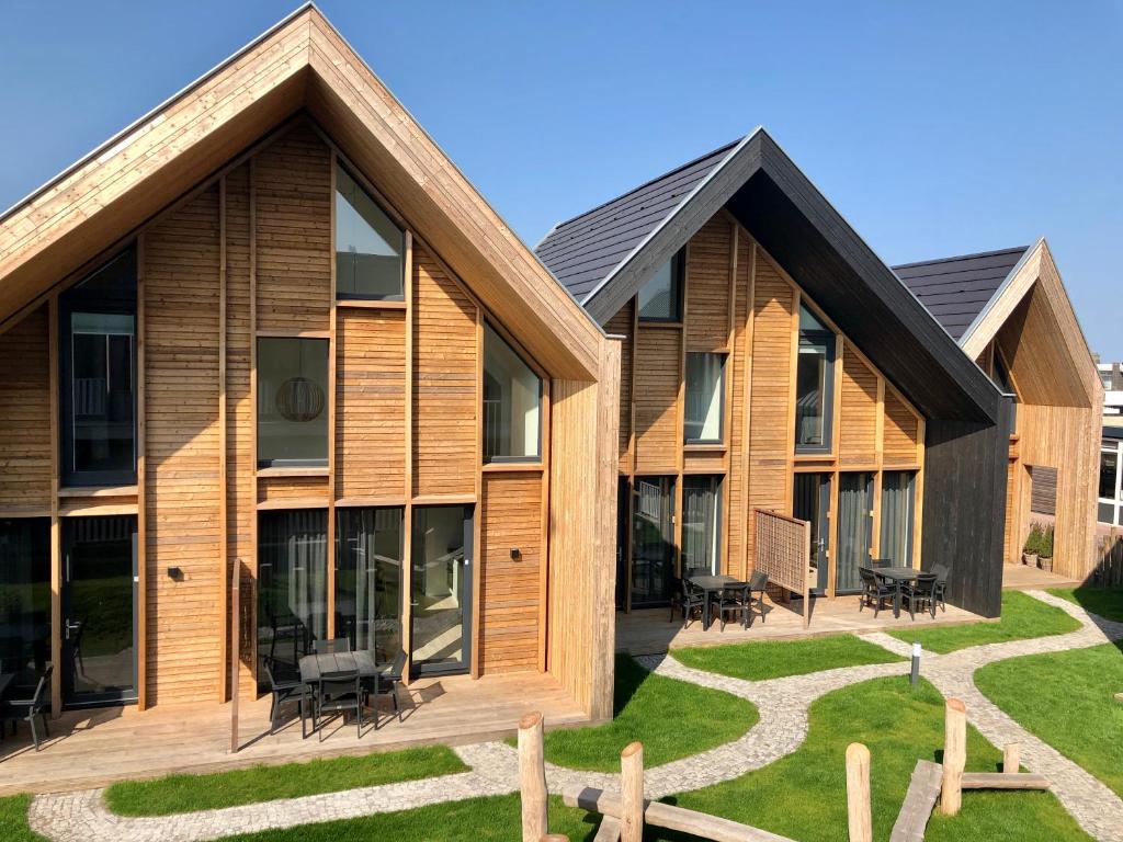 a house with wooden cladding and a lawn at Plein 40 - Lodges in Zoutelande