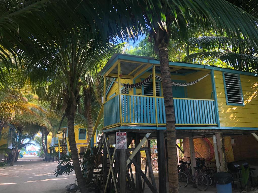 a yellow house with a blue balcony and palm trees at Colinda Cabanas in Caye Caulker