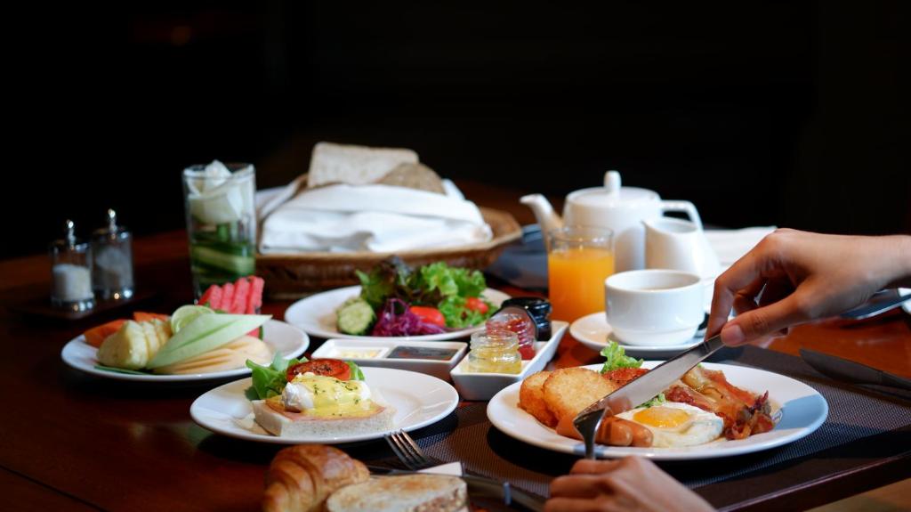 A breakfast table is set with eggs, sausage, salad, fruit, pastries, bread, and drinks.