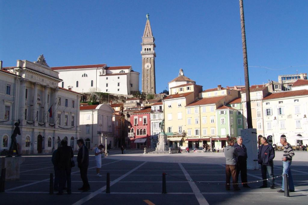 Un groupe de personnes debout sur une place avec une tour d'horloge dans l'établissement Apartments Piran, à Piran