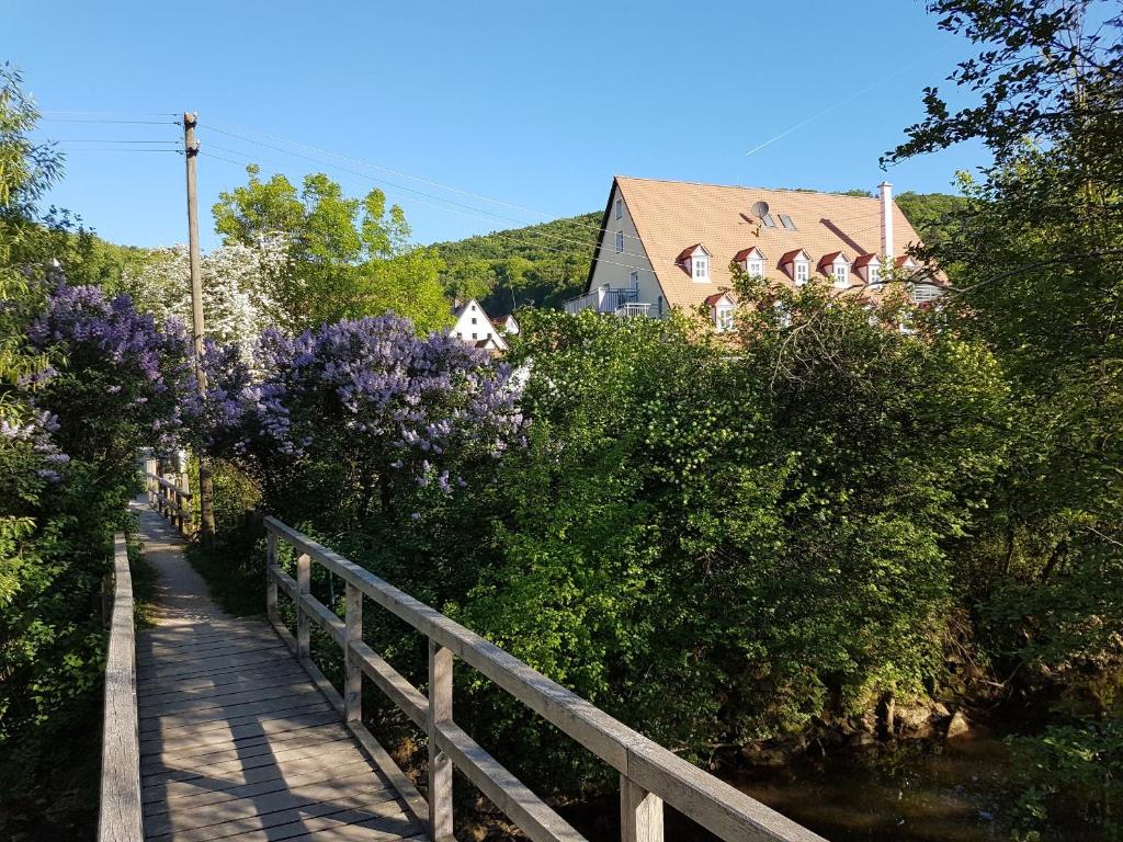 een houten brug met paarse bloemen en een huis bij Apartment Pegnitzmühle mit Pegnitzinsel in Vorra