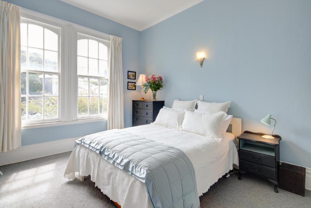 a blue bedroom with a bed and two windows at Thorndon Heritage Listed Villa in Wellington