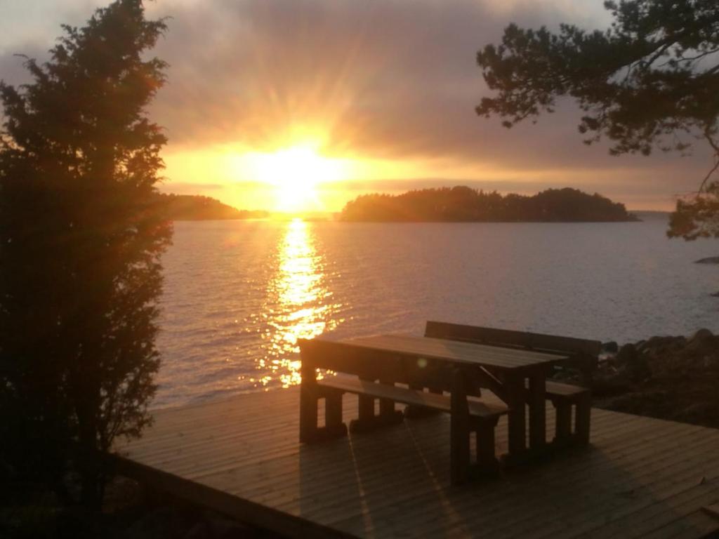 a bench sitting on a dock with the sunset in the background at Velkuanmaa Lomamökki in Naantali