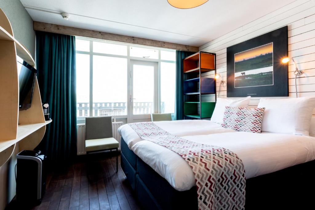 a hotel room with a bed and a large window at Strandhotel Westduin in Koudekerke